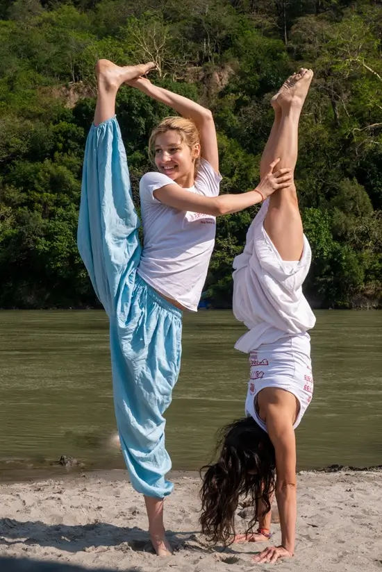 Two students practising a standing split and handstand on the Ganges bank, Rishikesh