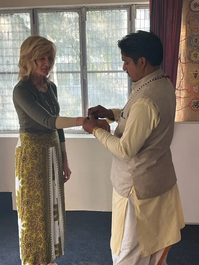 A teacher tying a thread at a student's wrist during a sankalpa ceremony