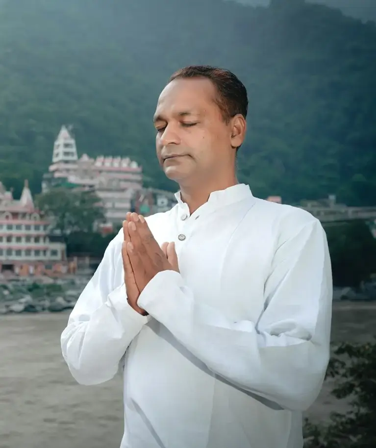 Sunil Sharma, founder of Yoganga Healing, standing in namaste above the Ganga at Rishikesh