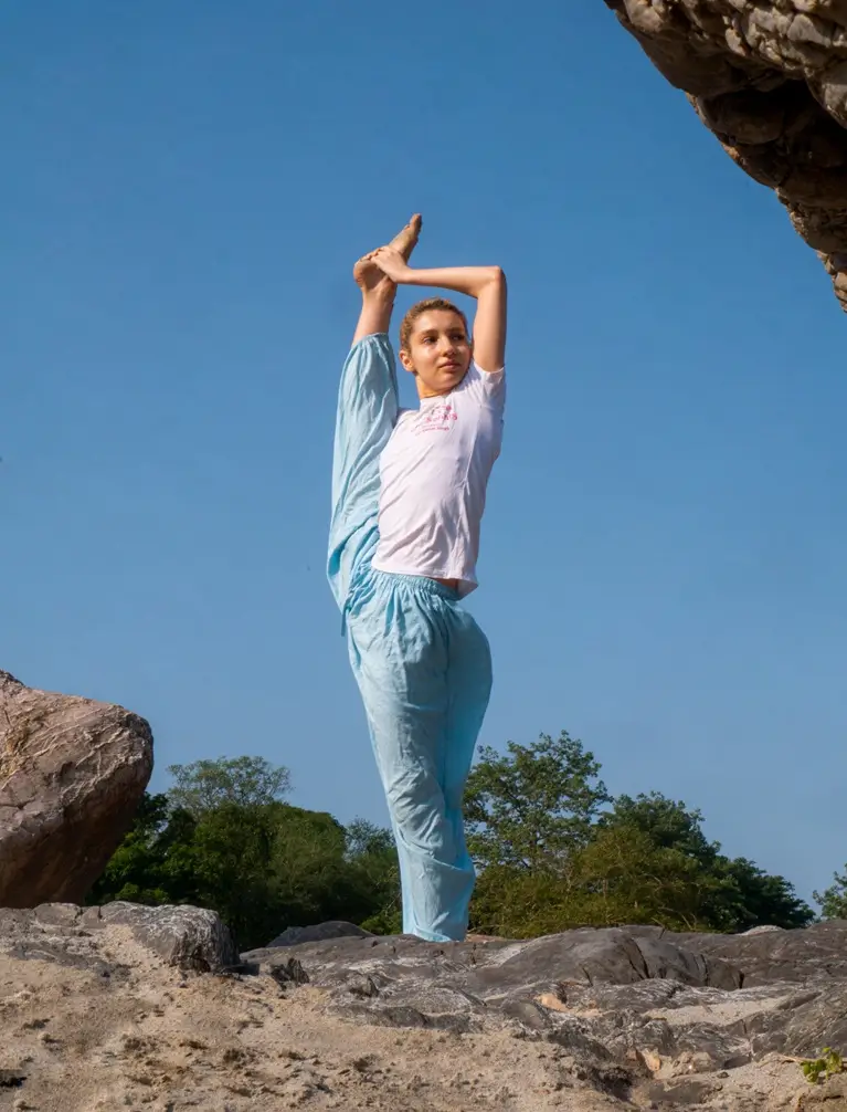 A student holding a standing balance on the rocks under an open sky in Rishikesh