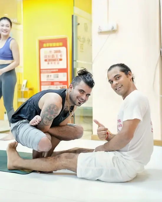 A teacher assisting a student through a seated forward fold